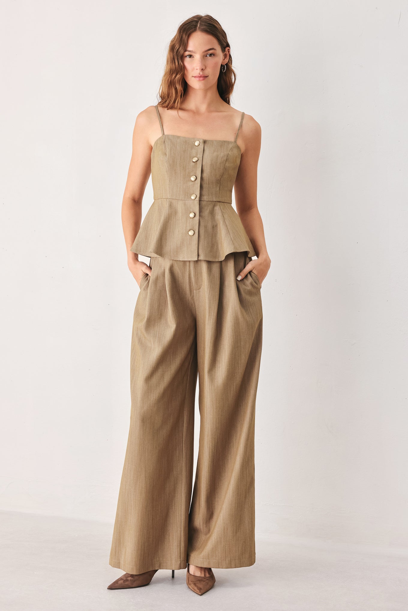 A woman wearing a tan linen camisole top with thin straps, a structured square neckline, peplum waist, and a front button closure | FREEMARKET