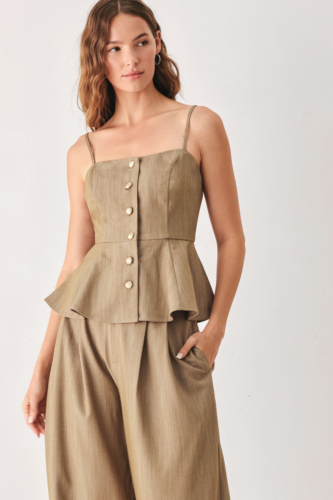 A woman wearing a tan linen camisole top with thin straps, a structured square neckline, peplum waist, and a front button closure | FREEMARKET