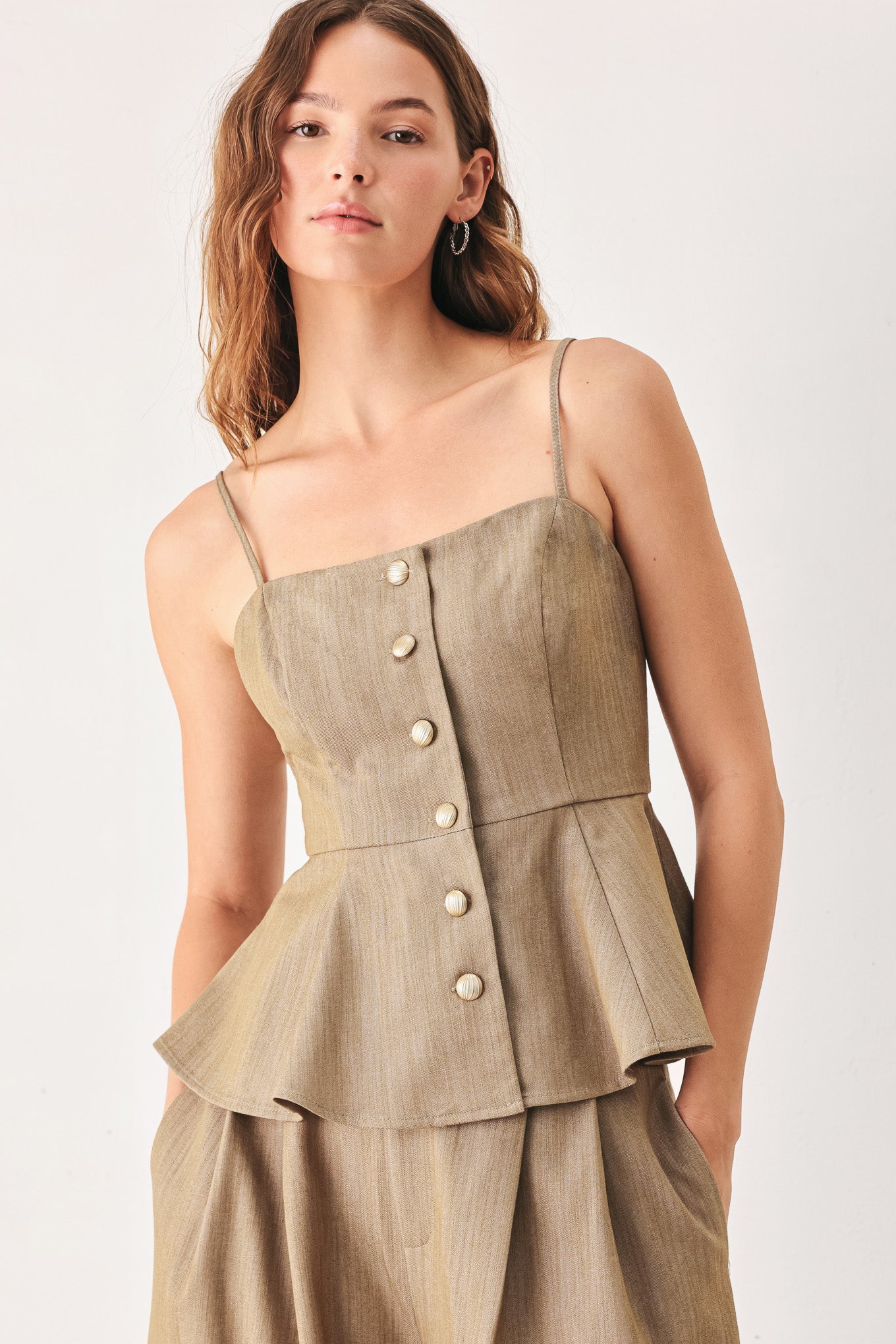 A woman wearing a tan linen camisole top with thin straps, a structured square neckline, peplum waist, and a front button closure | FREEMARKET