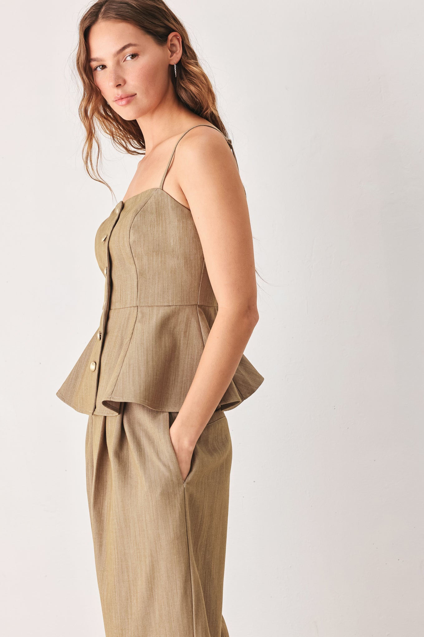 A woman wearing a tan linen camisole top with thin straps, a structured square neckline, peplum waist, and a front button closure | FREEMARKET