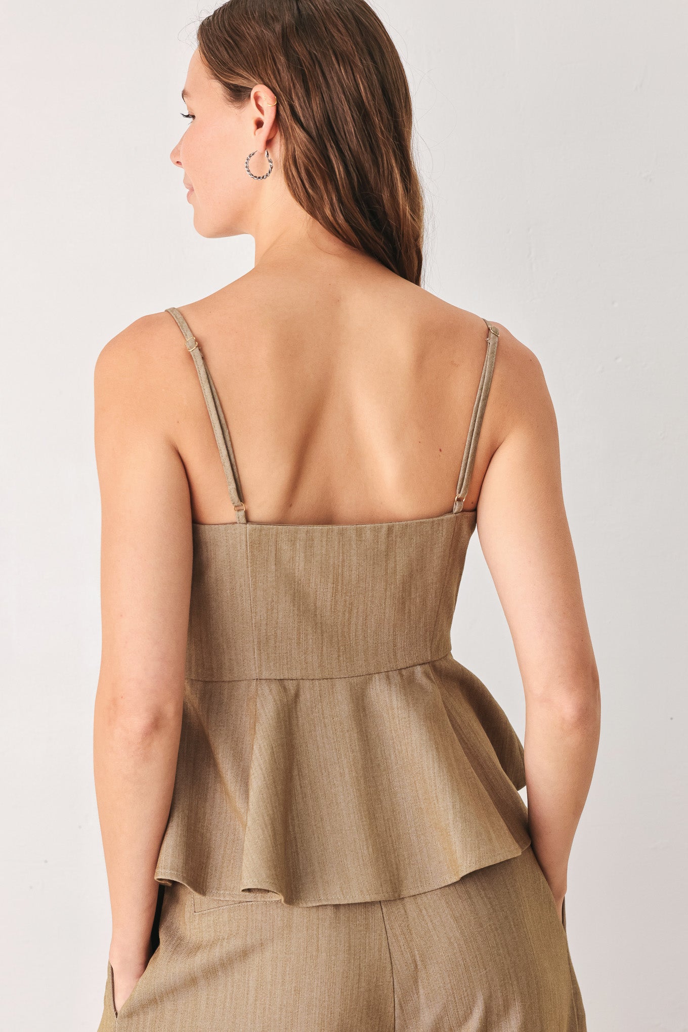 A woman wearing a tan linen camisole top with thin straps, a structured square neckline, peplum waist, and a front button closure | FREEMARKET