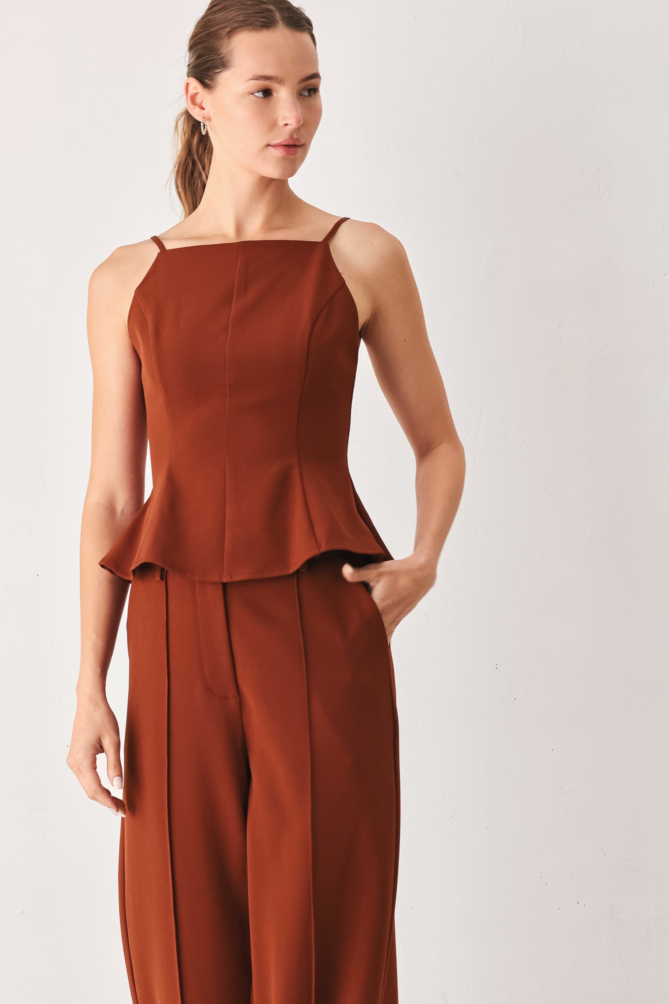 A woman wearing a rust-brown sleeveless peplum top | FREEMARKET