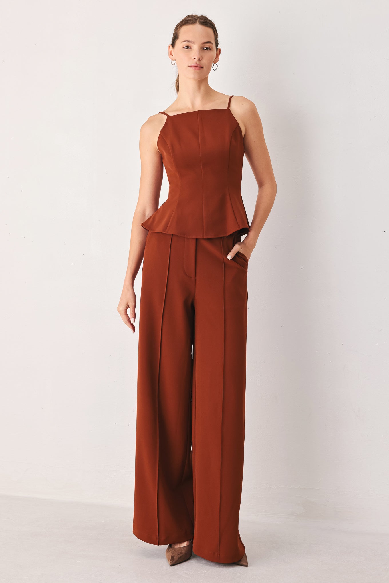A woman wearing a rust-brown sleeveless peplum top | FREEMARKET