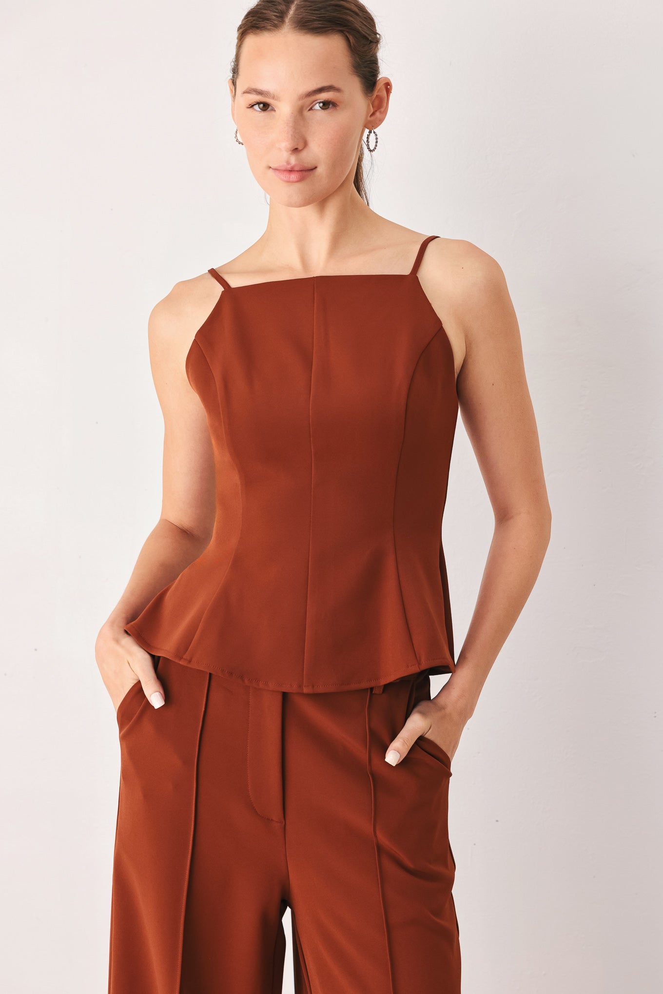 A woman wearing a rust-brown sleeveless peplum top | FREEMARKET