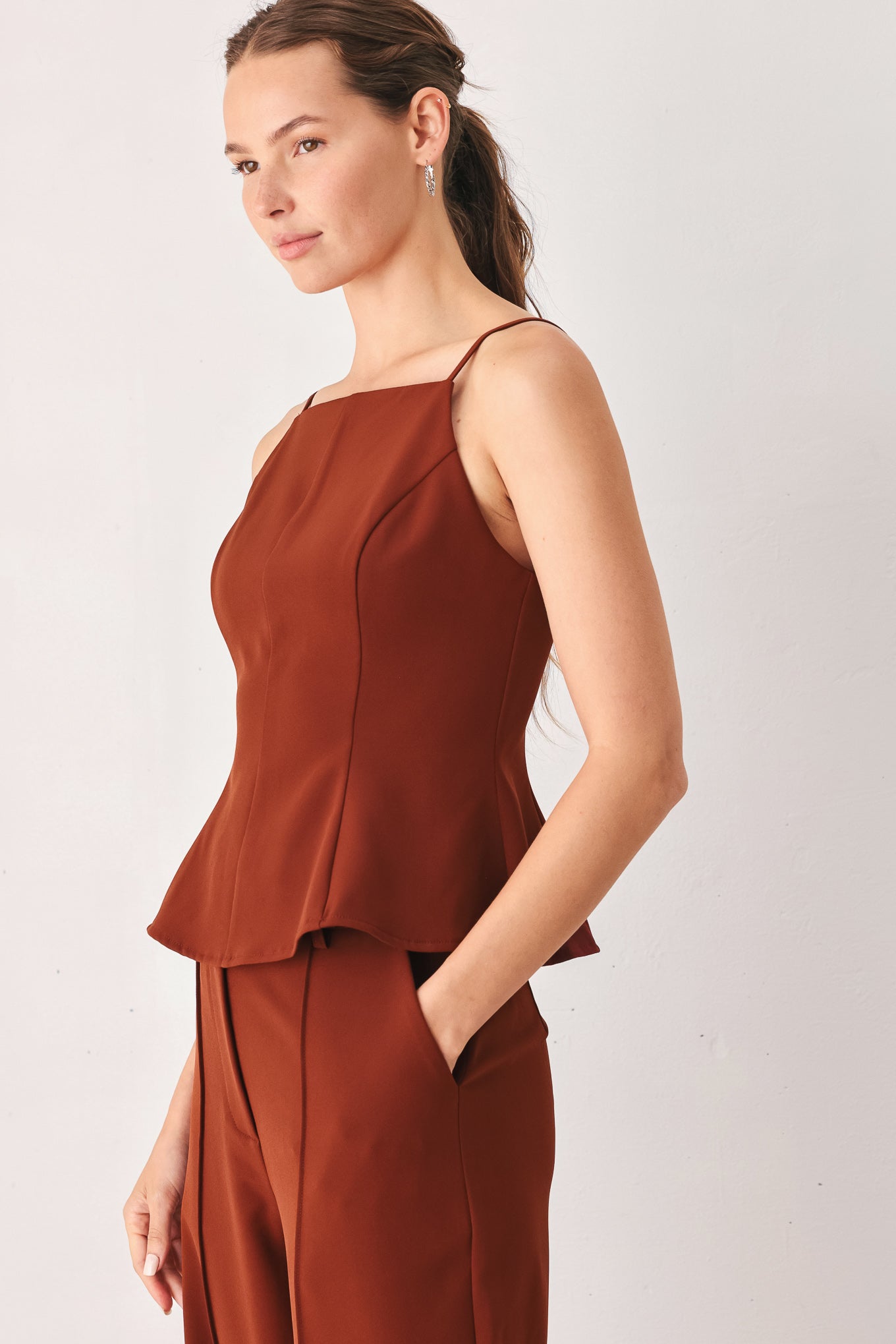 A woman wearing a rust-brown sleeveless peplum top | FREEMARKET