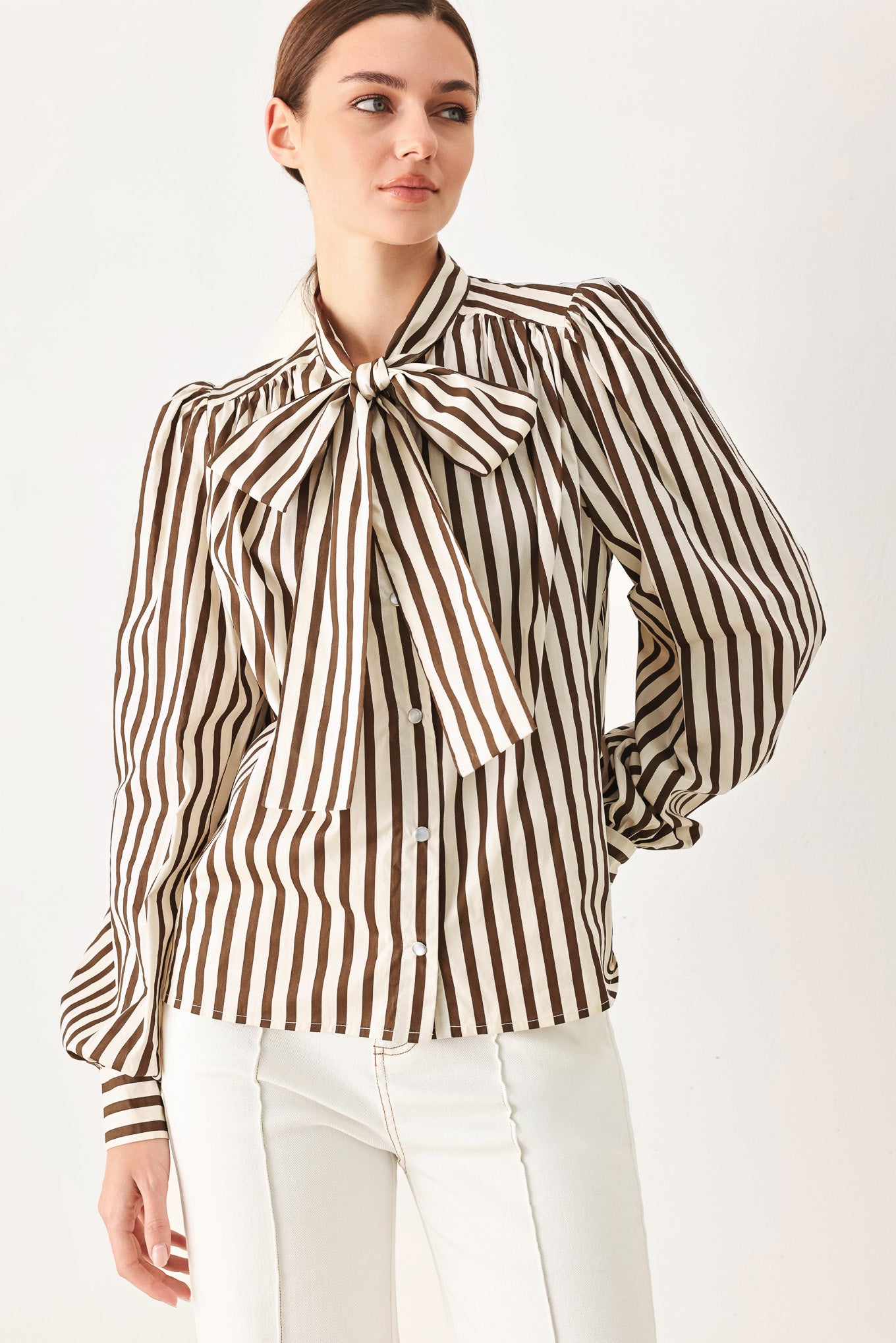 A woman wearing a brown and beige vertically striped long-sleeve blouse with a large bow at the collar | FREEMARKET