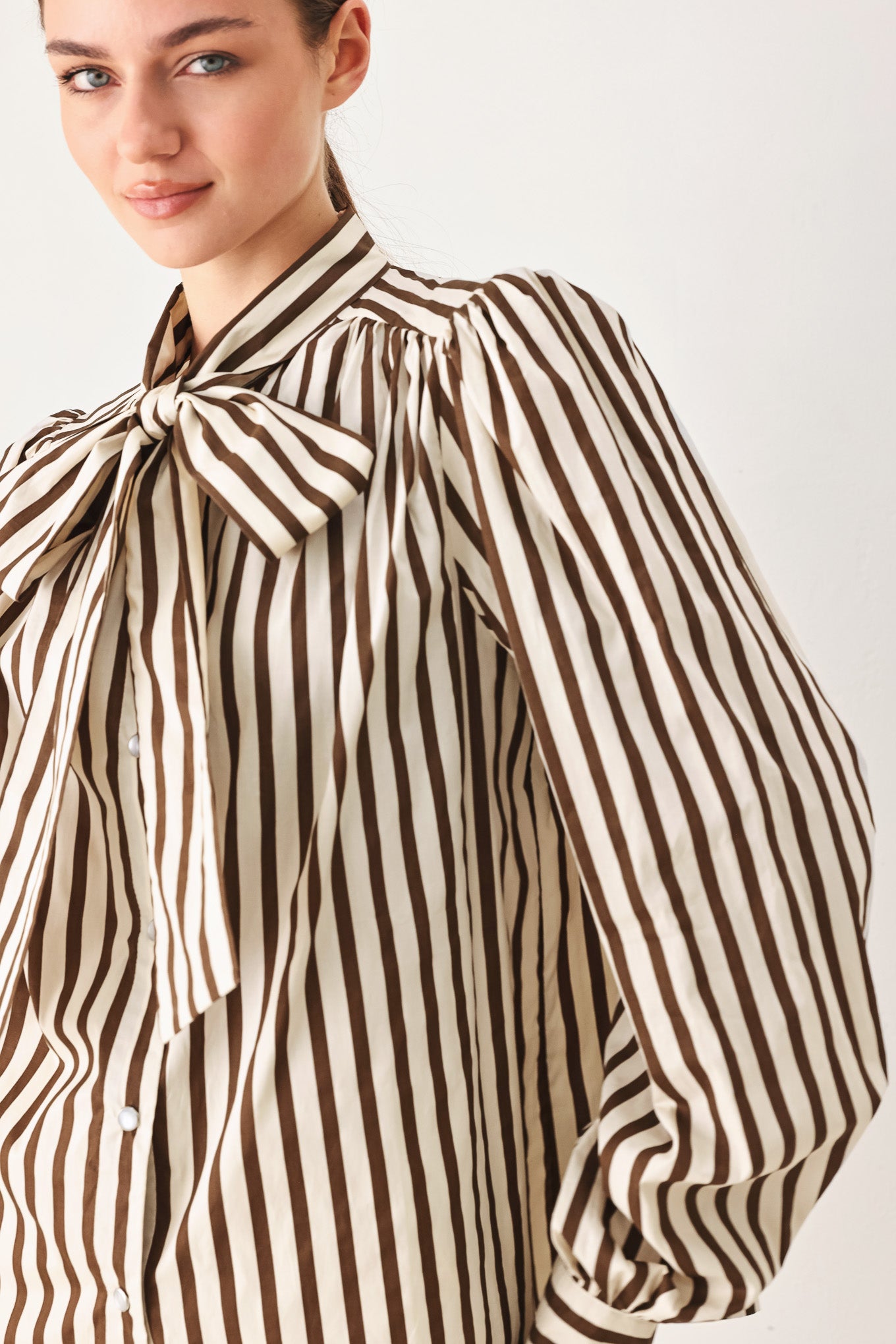 A woman wearing a brown and beige vertically striped long-sleeve blouse with a large bow at the collar | FREEMARKET