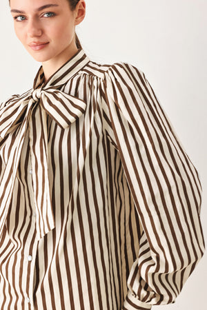 A woman wearing a brown and beige vertically striped long-sleeve blouse with a large bow at the collar | FREEMARKET