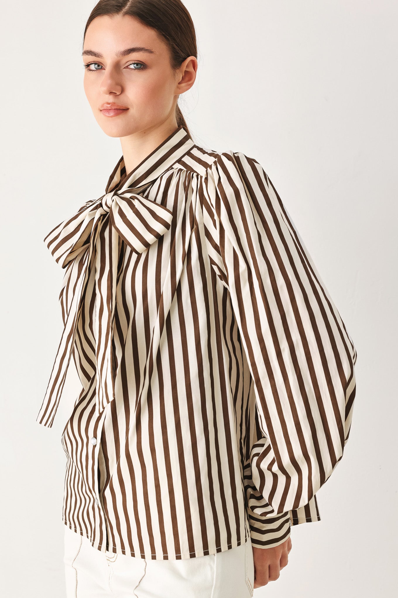 A woman wearing a brown and beige vertically striped long-sleeve blouse with a large bow at the collar | FREEMARKET