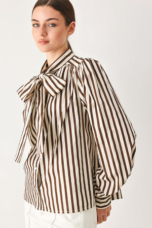 A woman wearing a brown and beige vertically striped long-sleeve blouse with a large bow at the collar | FREEMARKET