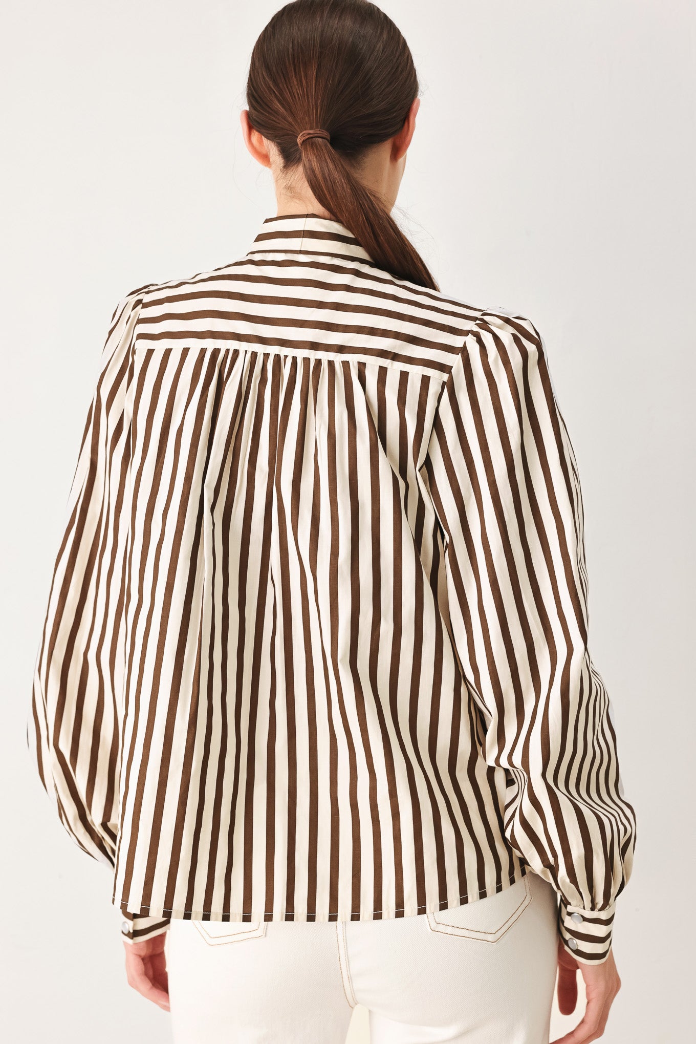 A woman wearing a brown and beige vertically striped long-sleeve blouse with a large bow at the collar | FREEMARKET