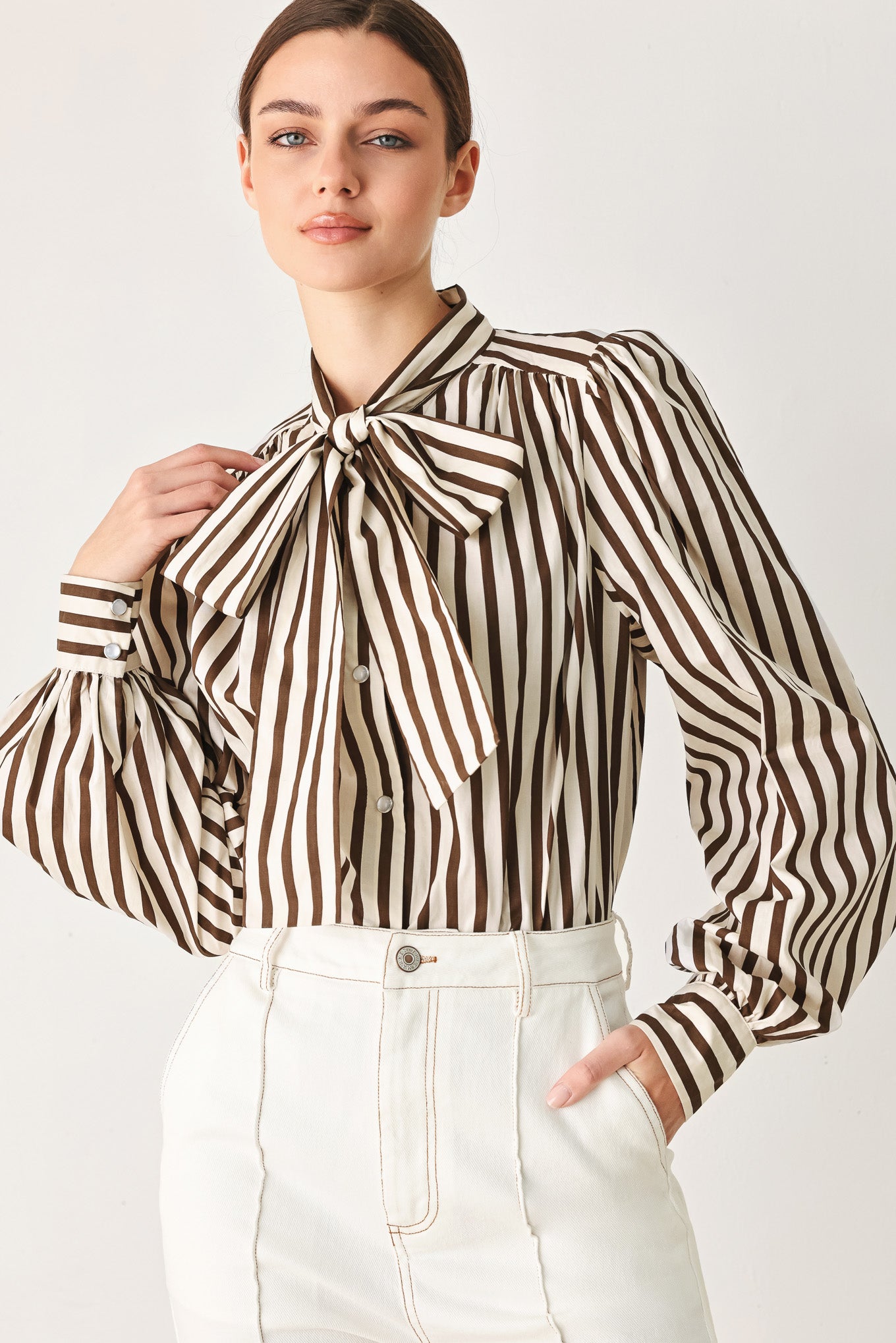 A woman wearing a brown and beige vertically striped long-sleeve blouse with a large bow at the collar | FREEMARKET