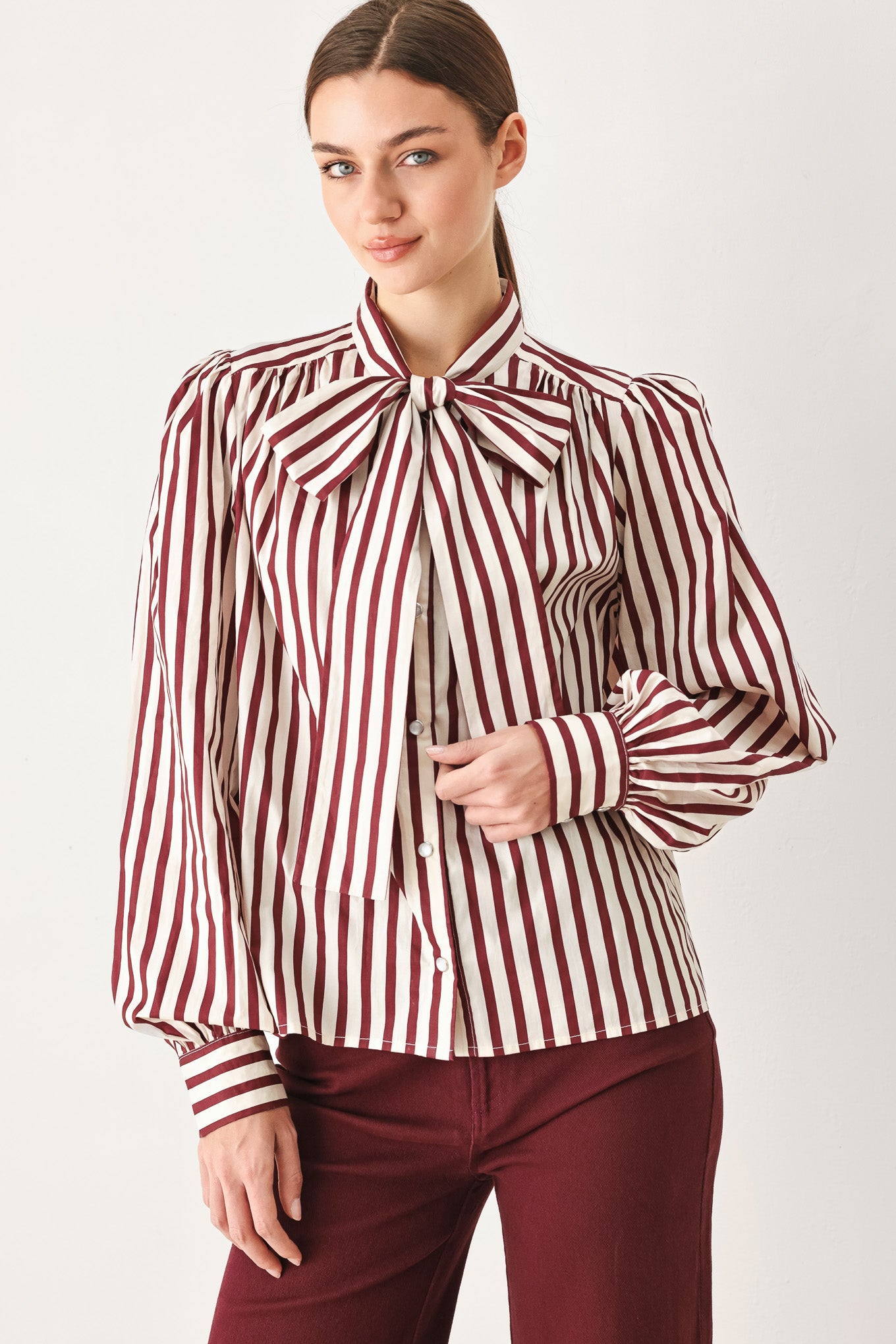 A woman wearing a burgundy and beige vertically striped long-sleeve blouse with a large bow at the collar | FREEMARKET