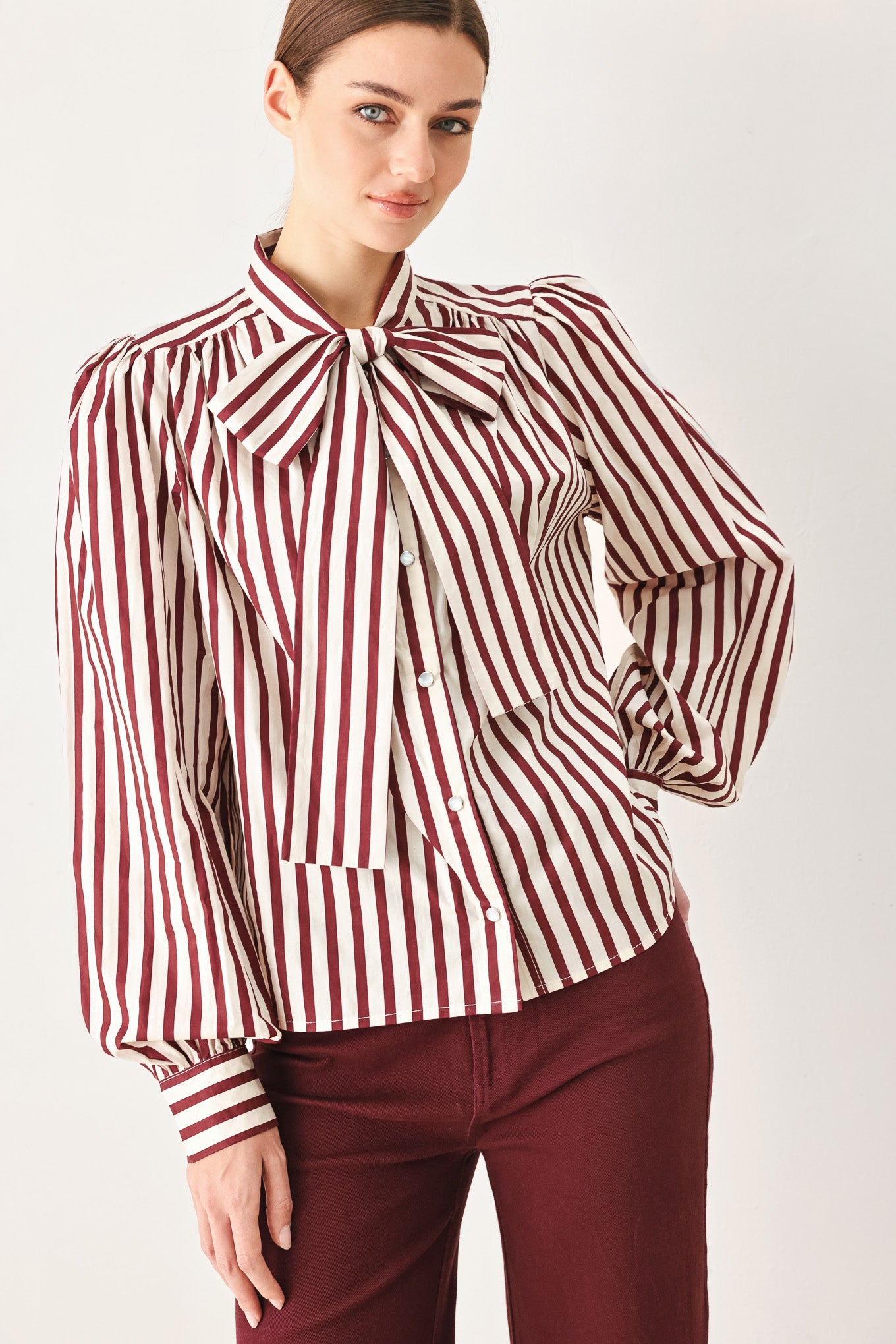 A woman wearing a burgundy and beige vertically striped long-sleeve blouse with a large bow at the collar | FREEMARKET