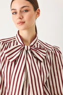 A woman wearing a burgundy and beige vertically striped long-sleeve blouse with a large bow at the collar | FREEMARKET