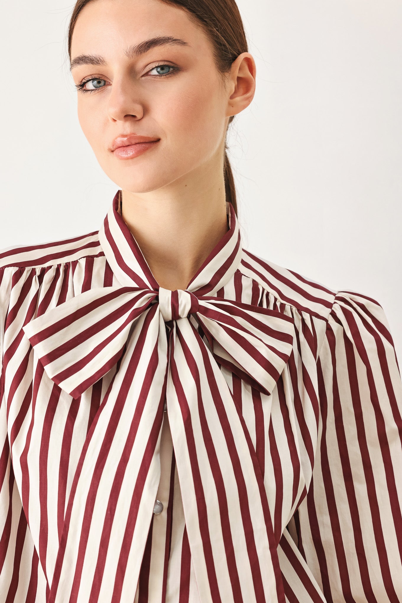 A woman wearing a burgundy and beige vertically striped long-sleeve blouse with a large bow at the collar | FREEMARKET