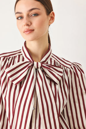 A woman wearing a burgundy and beige vertically striped long-sleeve blouse with a large bow at the collar | FREEMARKET