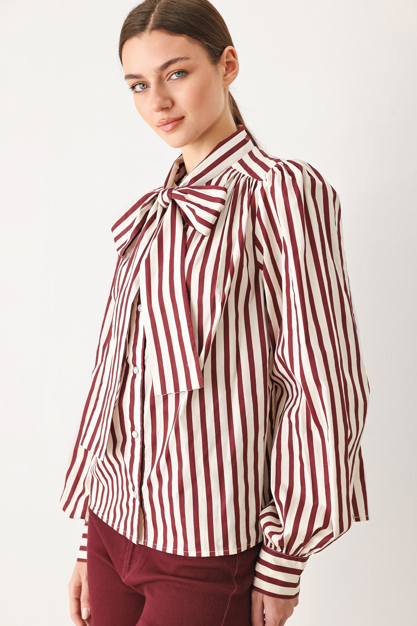 A woman wearing a burgundy and beige vertically striped long-sleeve blouse with a large bow at the collar | FREEMARKET