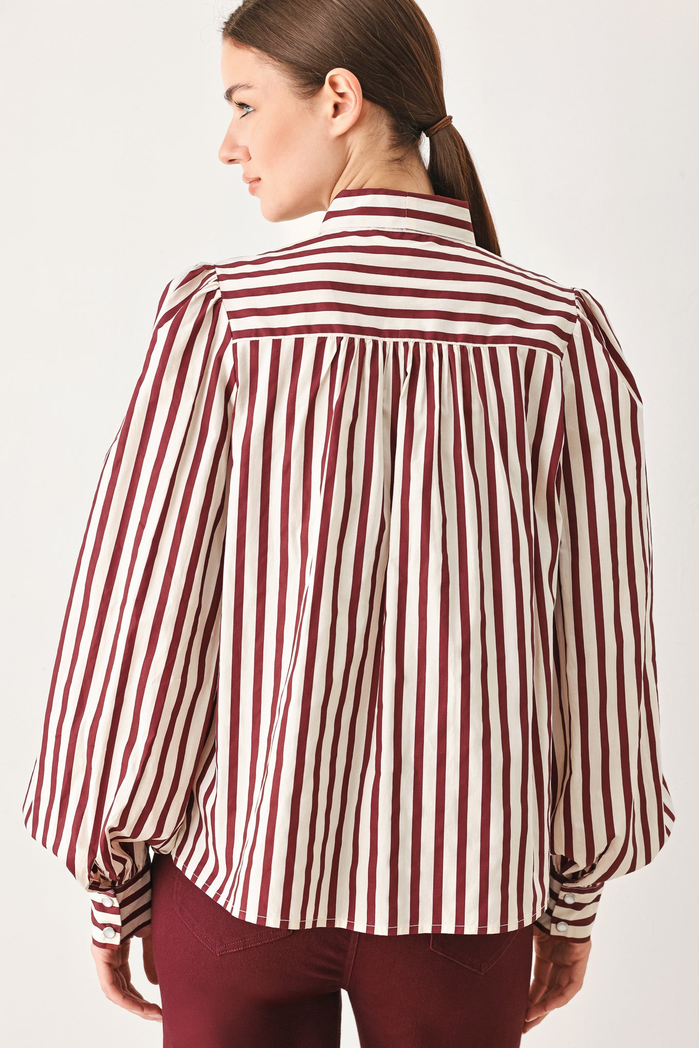 A woman wearing a burgundy and beige vertically striped long-sleeve blouse with a large bow at the collar | FREEMARKET