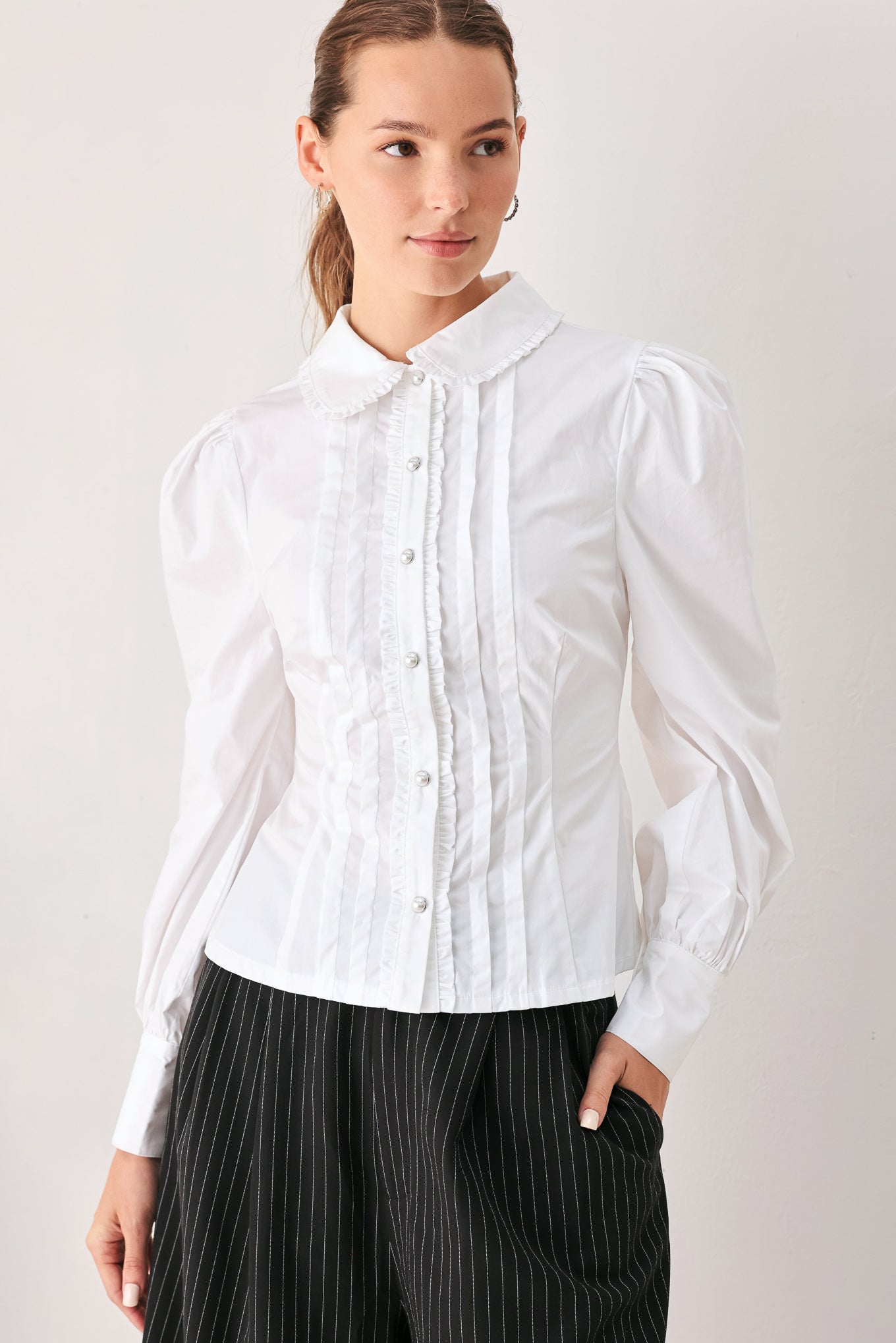 A woman wearing a white long-sleeve blouse with a high collar, decorative front pleats, and puffed shoulders | FREEMARKET