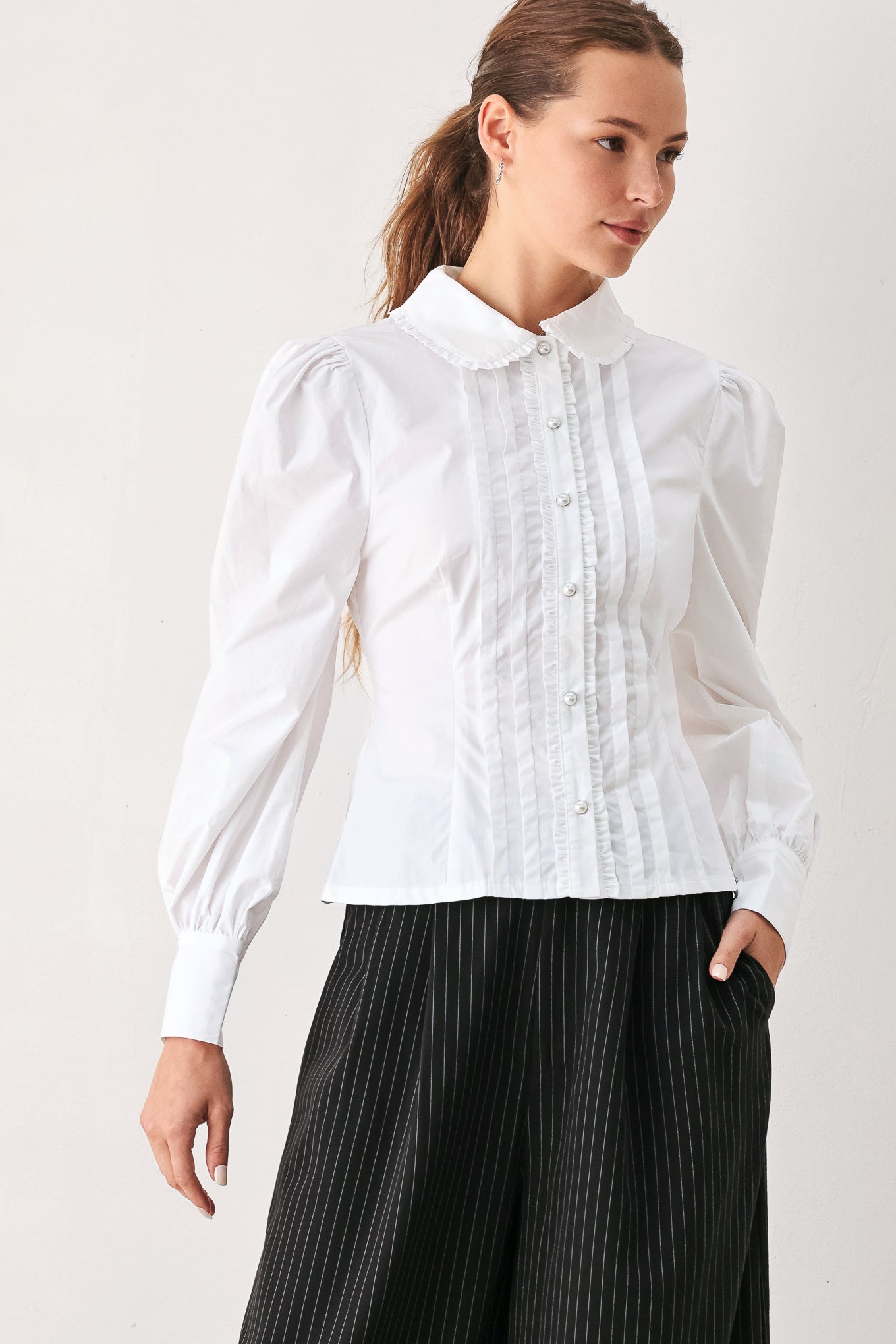 A woman wearing a white long-sleeve blouse with a high collar, decorative front pleats, and puffed shoulders | FREEMARKET