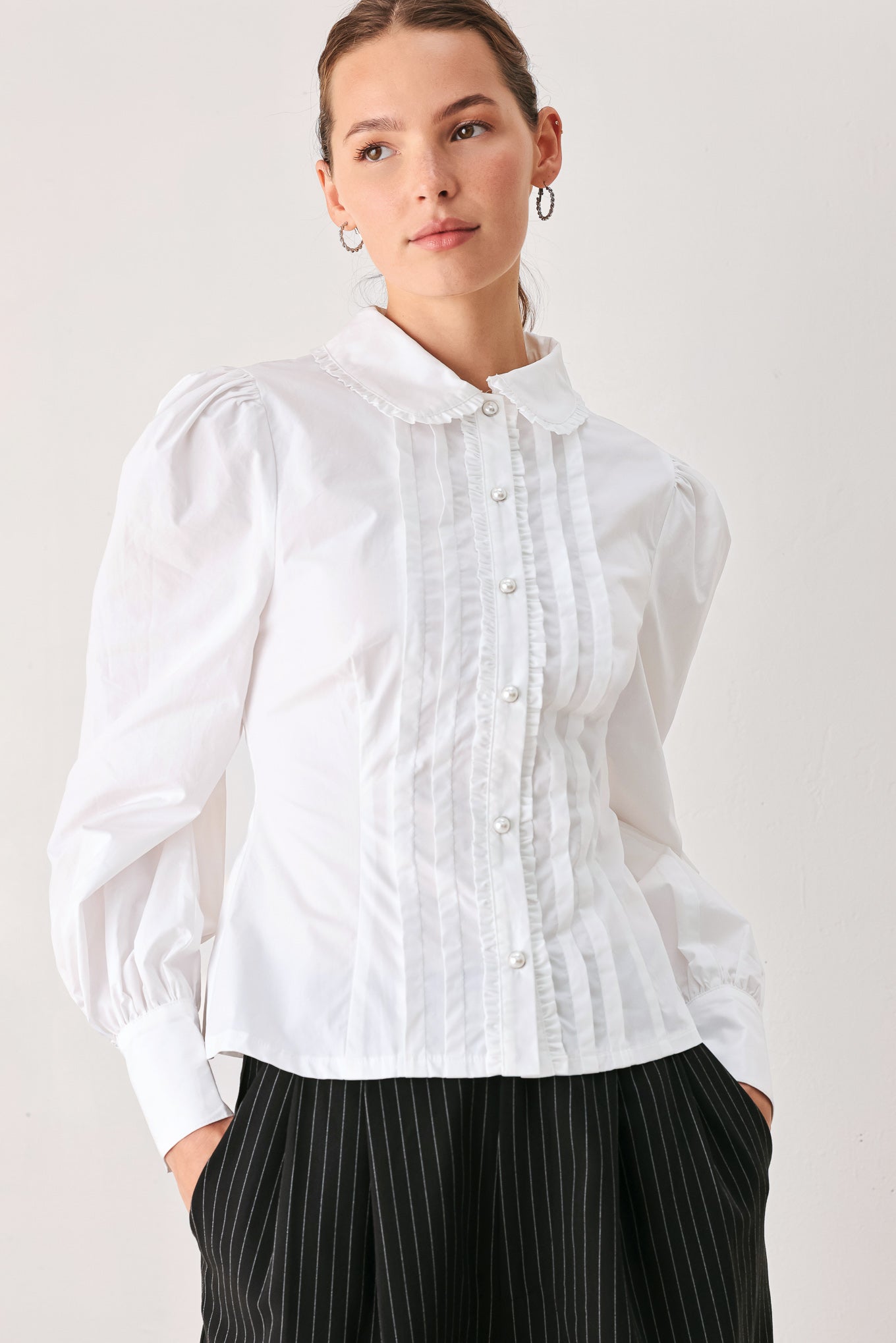 A woman wearing a white long-sleeve blouse with a high collar, decorative front pleats, and puffed shoulders | FREEMARKET