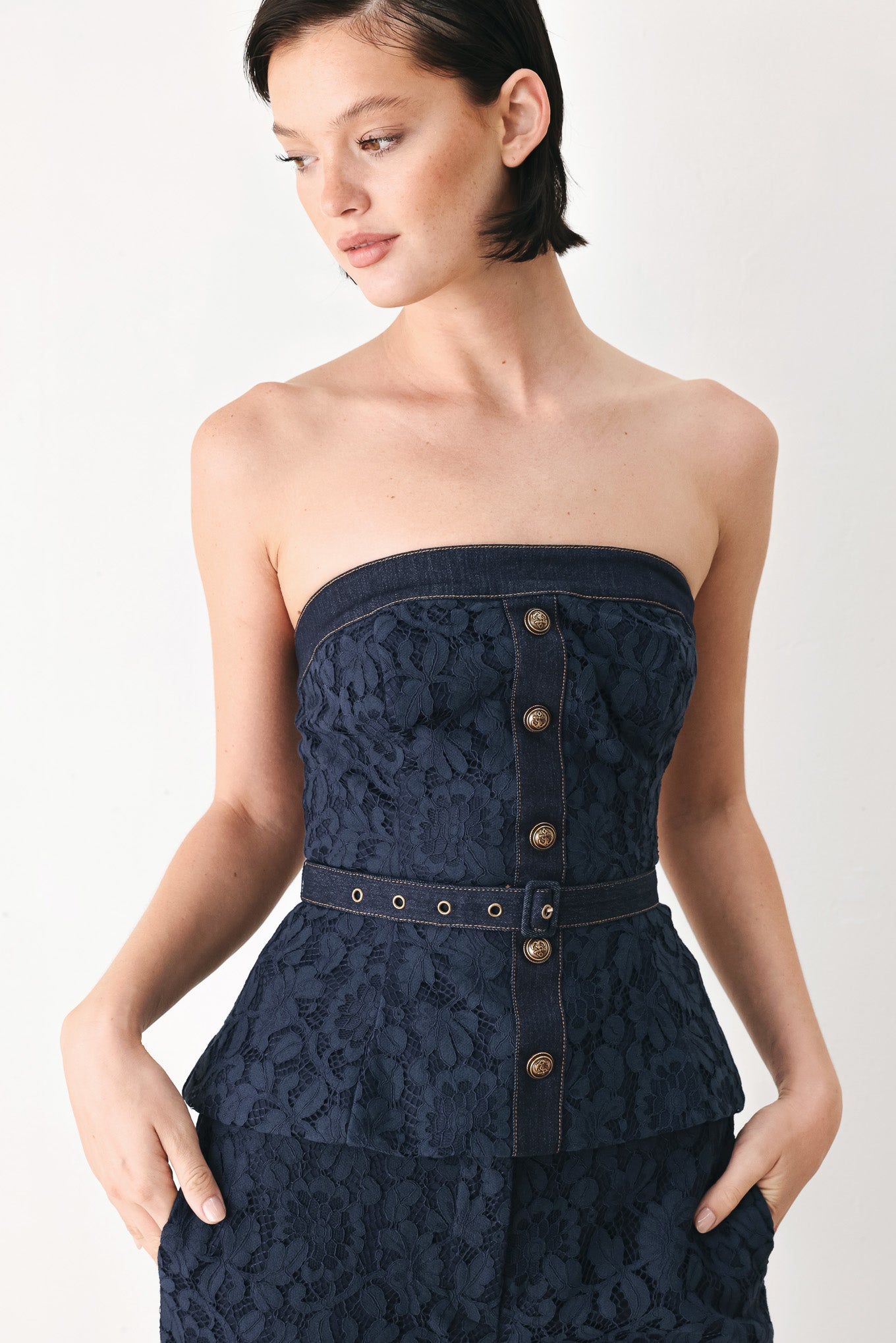 A woman wearing a strapless dark navy blue textured dress with a buttoned waist and a matching belt | FREEMARKET