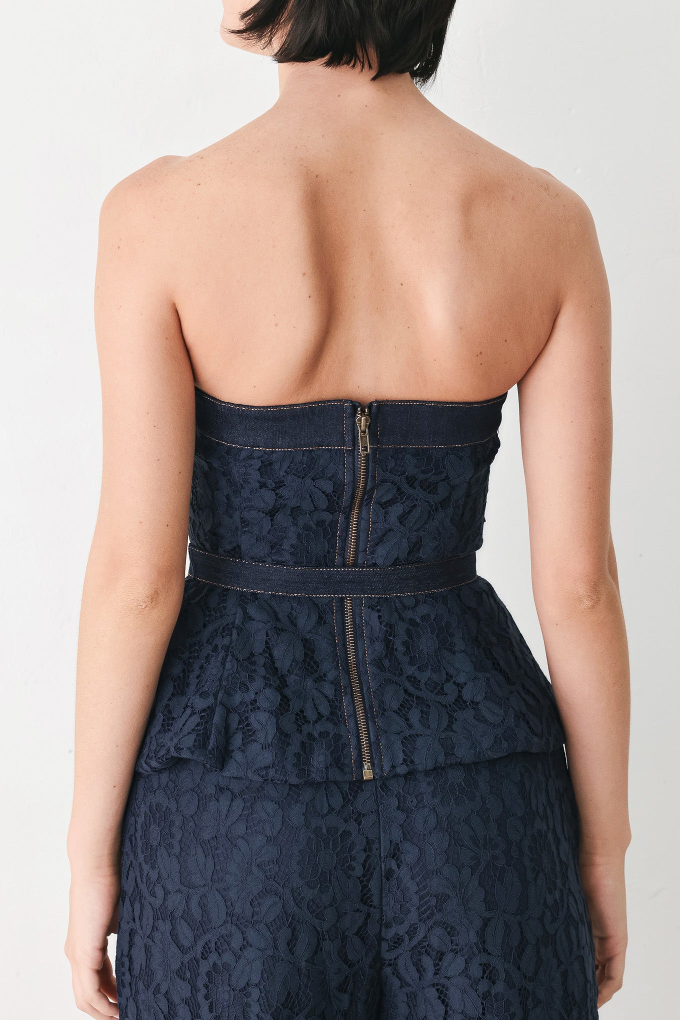A woman wearing a strapless dark navy blue textured dress with a buttoned waist and a matching belt | FREEMARKET