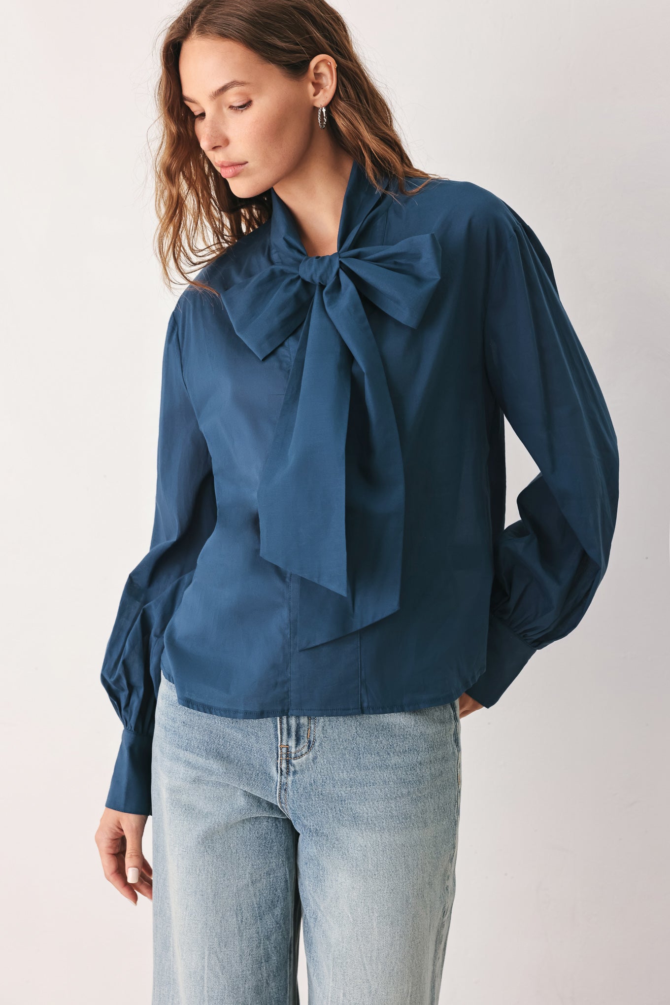 A woman wearing a dark navy blue long-sleeve blouse with a large bow at the collar | FREEMARKET