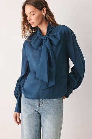 A woman wearing a dark navy blue long-sleeve blouse with a large bow at the collar | FREEMARKET