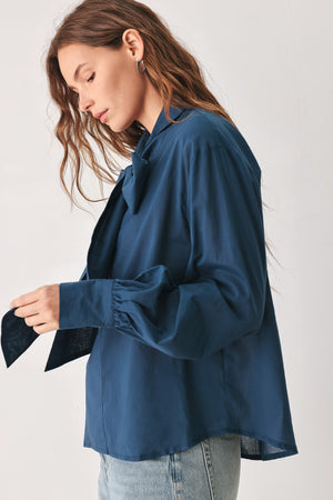 A woman wearing a dark navy blue long-sleeve blouse with a large bow at the collar | FREEMARKET