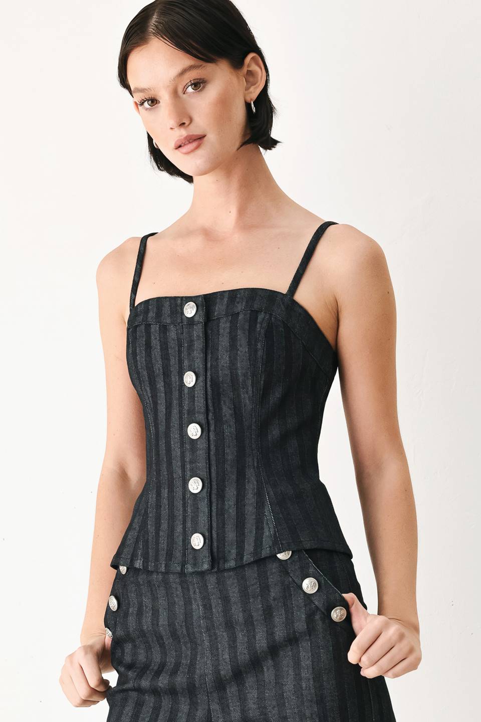 A model wearing a dark gray pinstriped jumpsuit with a structured corset-style bodice, thin shoulder straps, and prominent silver-tone decorative buttons down the front and on the waist | FREEMARKET