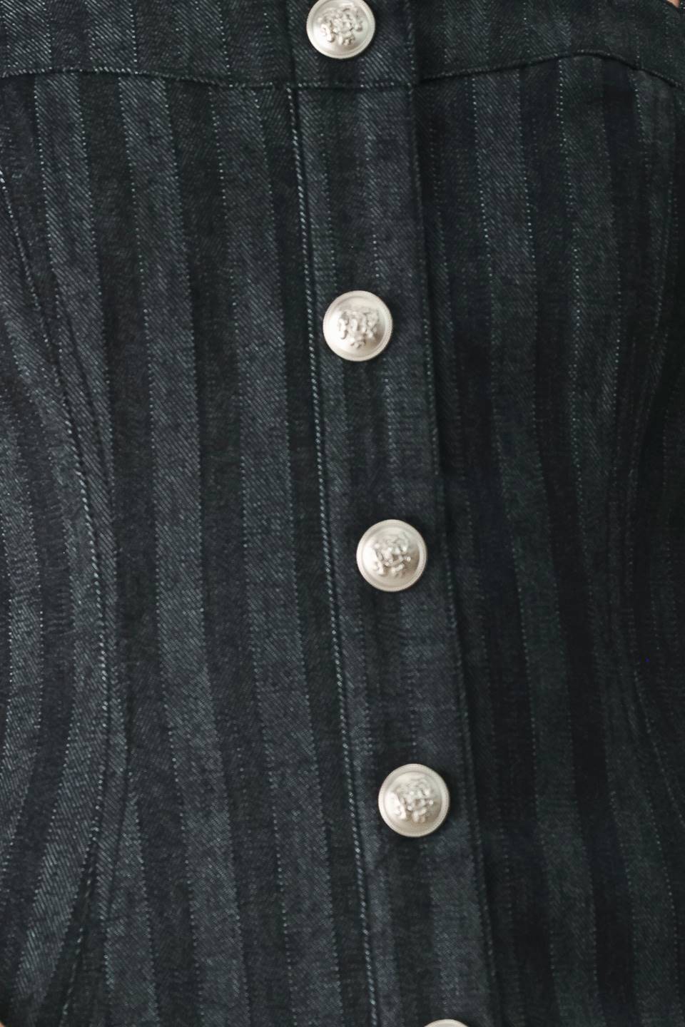 A model wearing a dark gray pinstriped jumpsuit with a structured corset-style bodice, thin shoulder straps, and prominent silver-tone decorative buttons down the front and on the waist | FREEMARKET