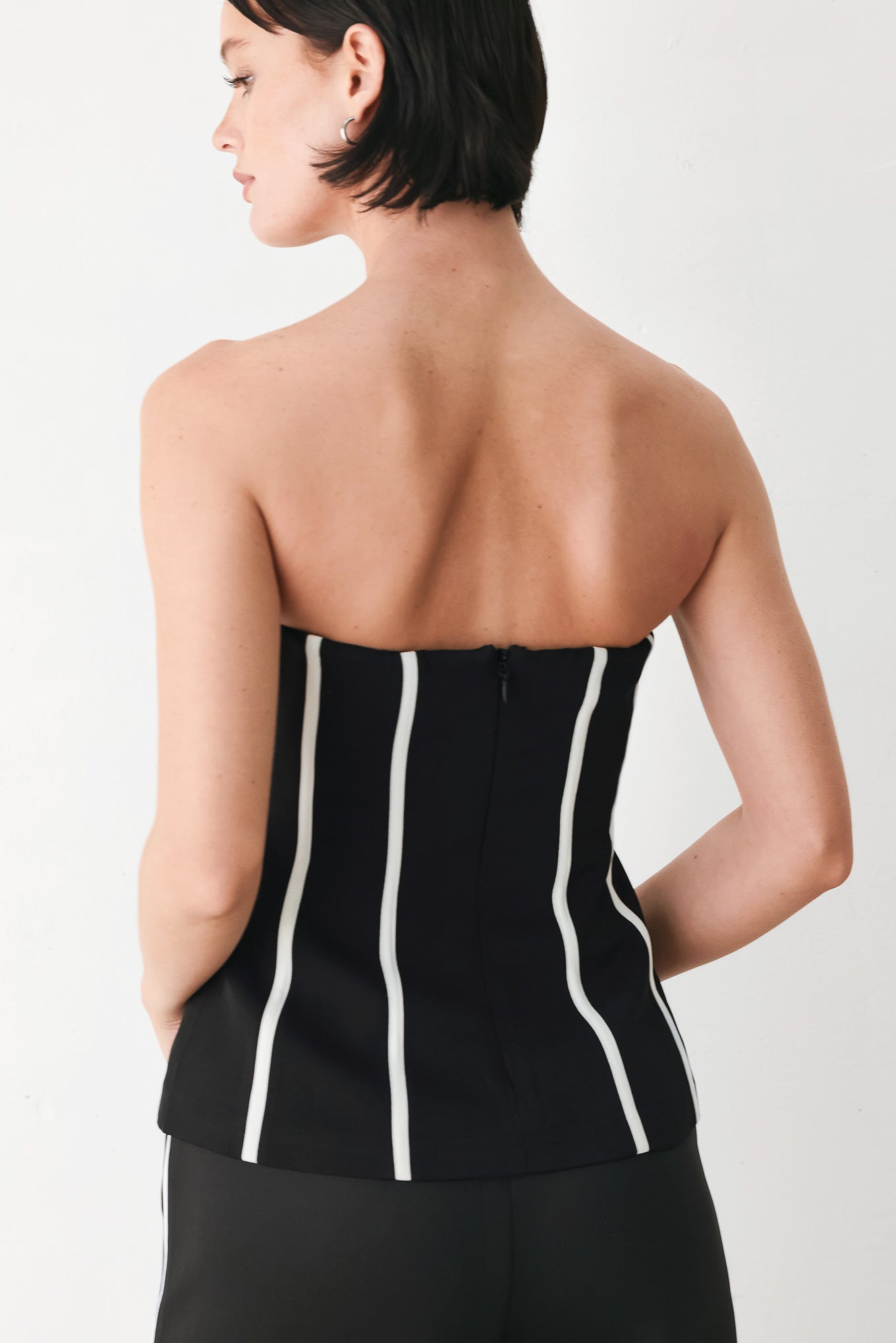 A woman wearing a strapless black corset-style top with bold white vertical stripes | FREEMARKET