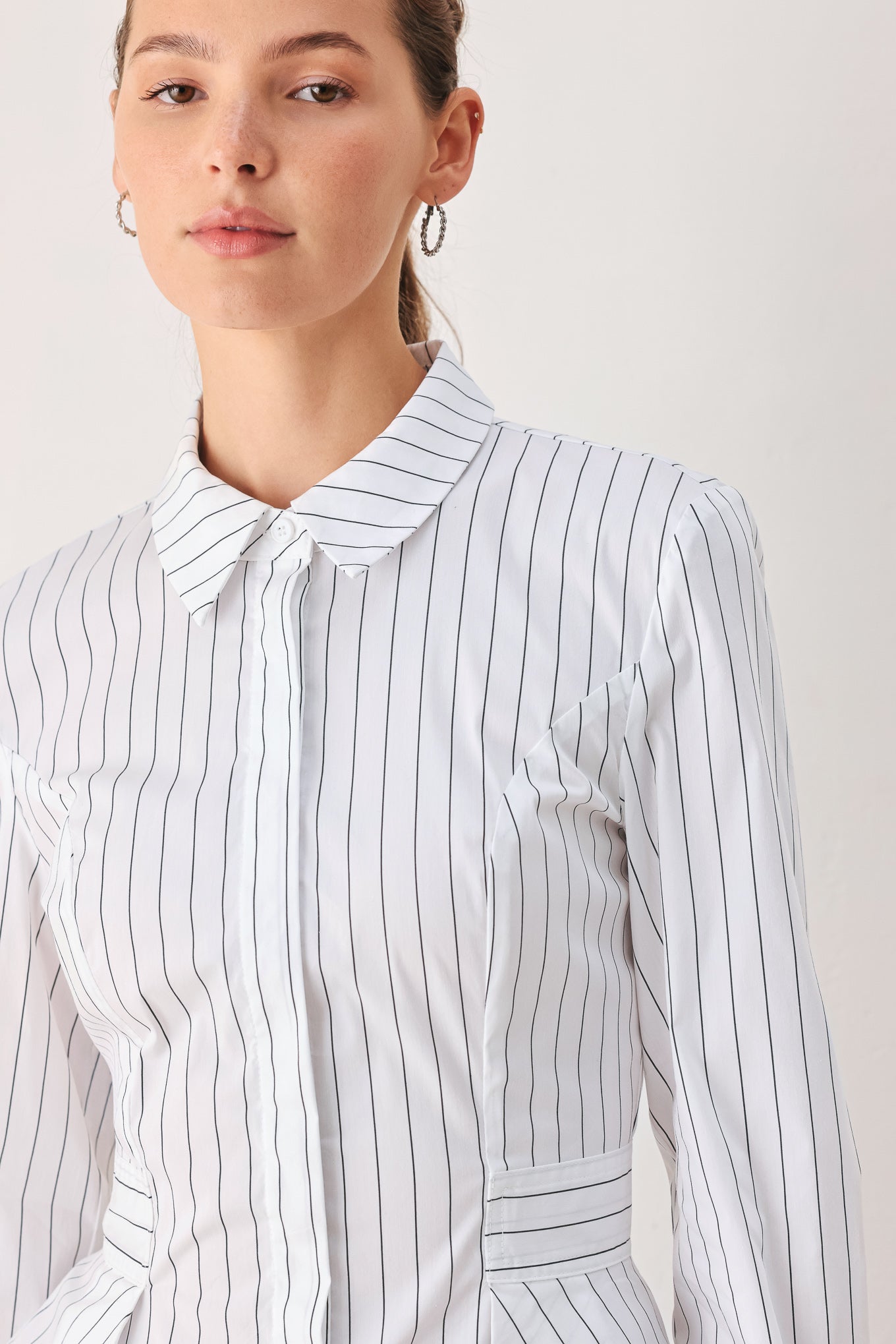 A woman wearing a white long-sleeve button-up shirt with thin vertical black stripes| FREEMARKET