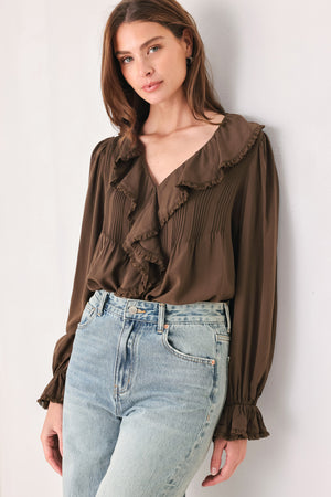 A woman wearing a brown long-sleeve blouse with pleated detailing and layered ruffles on the front | FREEMARKET
