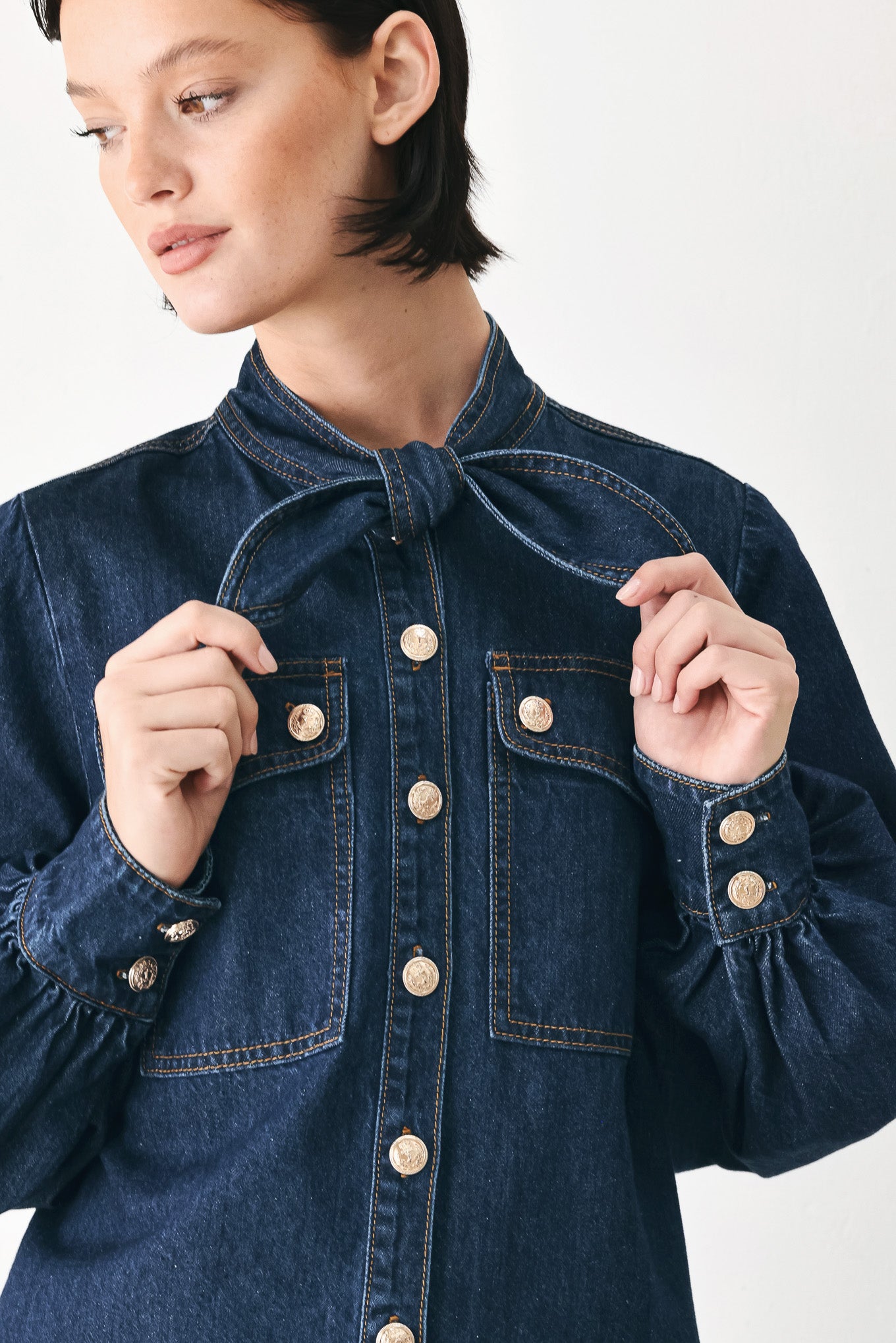 A close-up of a model wearing a dark blue denim shirt jacket with gold-tone buttons and a bow detail at the collar | FREEMARKET