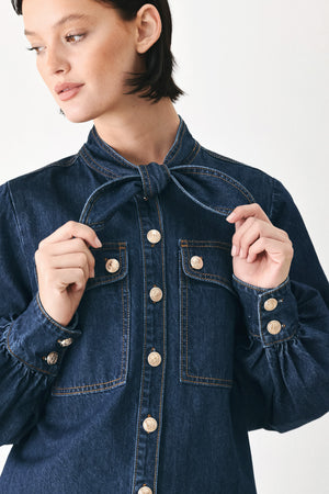 A close-up of a model wearing a dark blue denim shirt jacket with gold-tone buttons and a bow detail at the collar | FREEMARKET