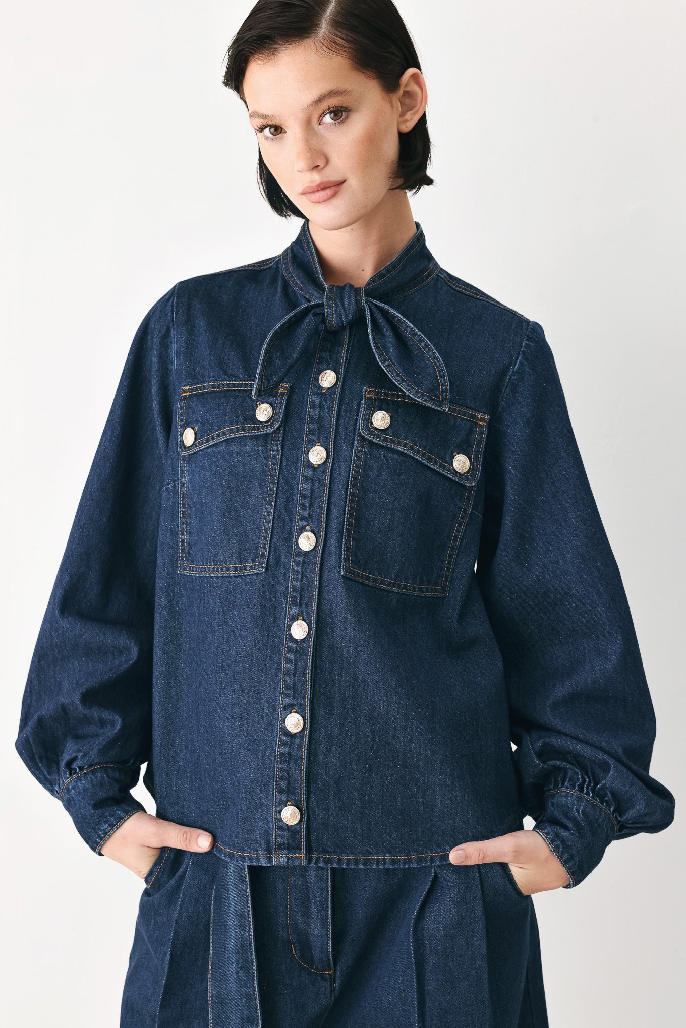 A model wearing a dark blue denim shirt jacket with gold-tone buttons and a bow detail at the collar | FREEMARKET