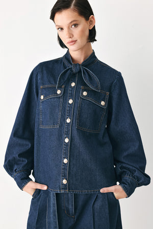 A model wearing a dark blue denim shirt jacket with gold-tone buttons and a bow detail at the collar | FREEMARKET