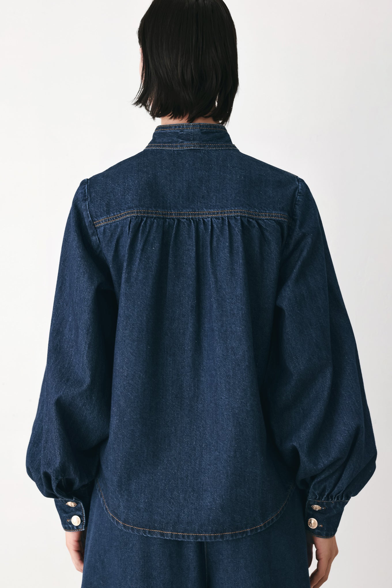 A model wearing a dark blue denim shirt jacket with gold-tone buttons and a bow detail at the collar | FREEMARKET