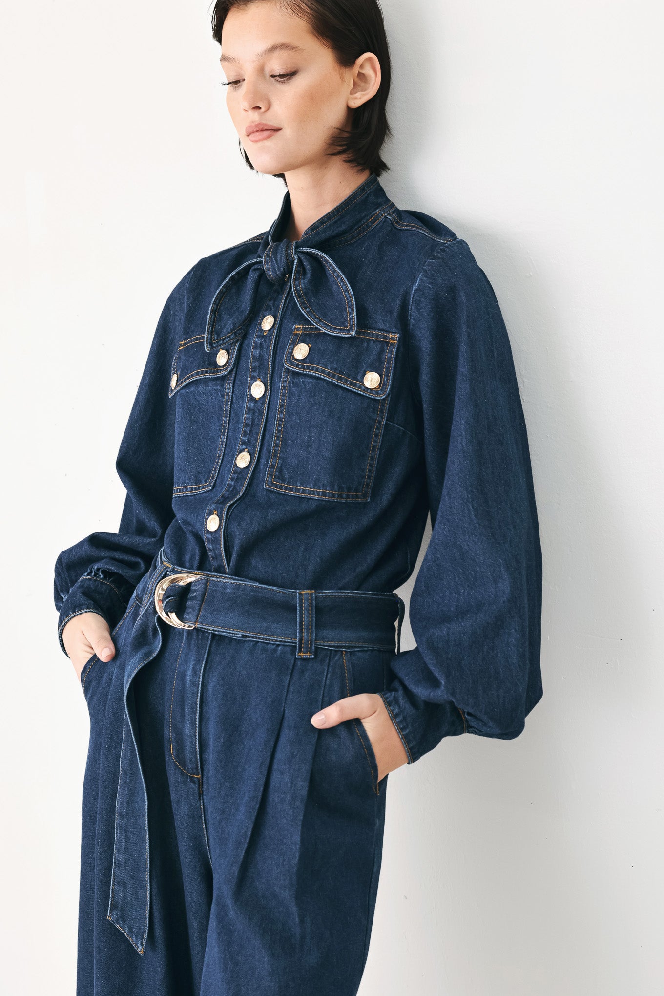 A model wearing a dark blue denim shirt jacket with gold-tone buttons and a bow detail at the collar | FREEMARKET