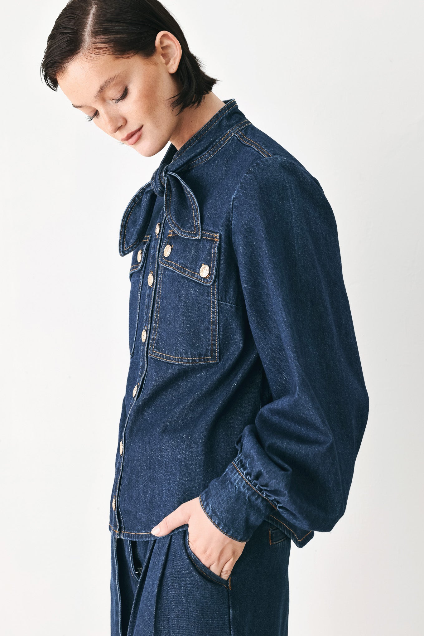 A model wearing a dark blue denim shirt jacket with gold-tone buttons and a bow detail at the collar | FREEMARKET