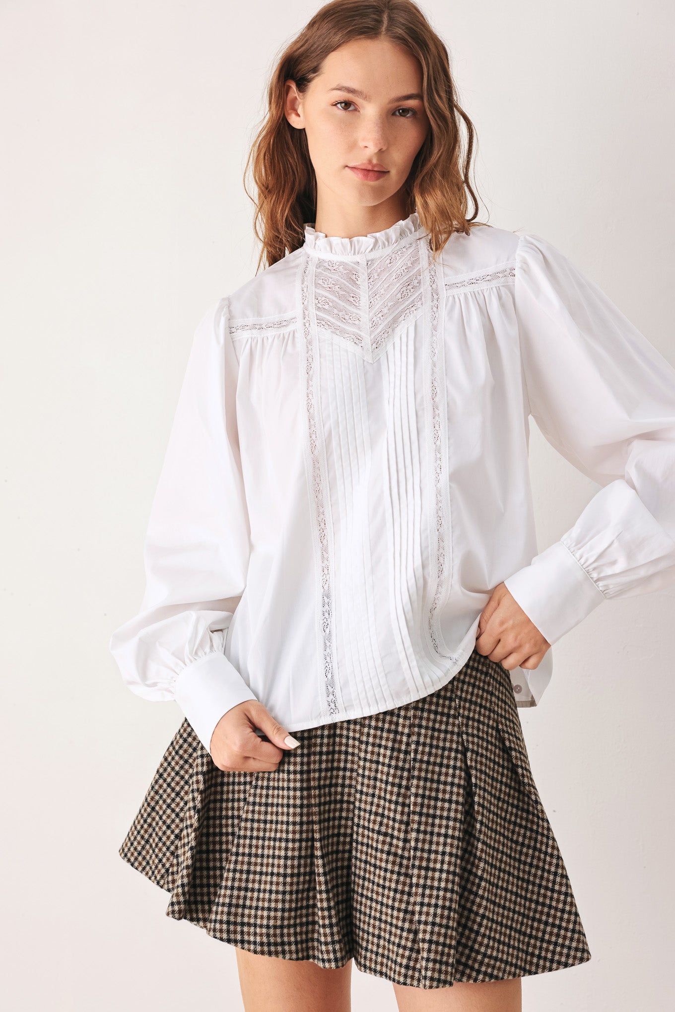 A woman modeling a white long-sleeve blouse with a ruffled high neck, pleated front, and lace detailing | FREEMARKET