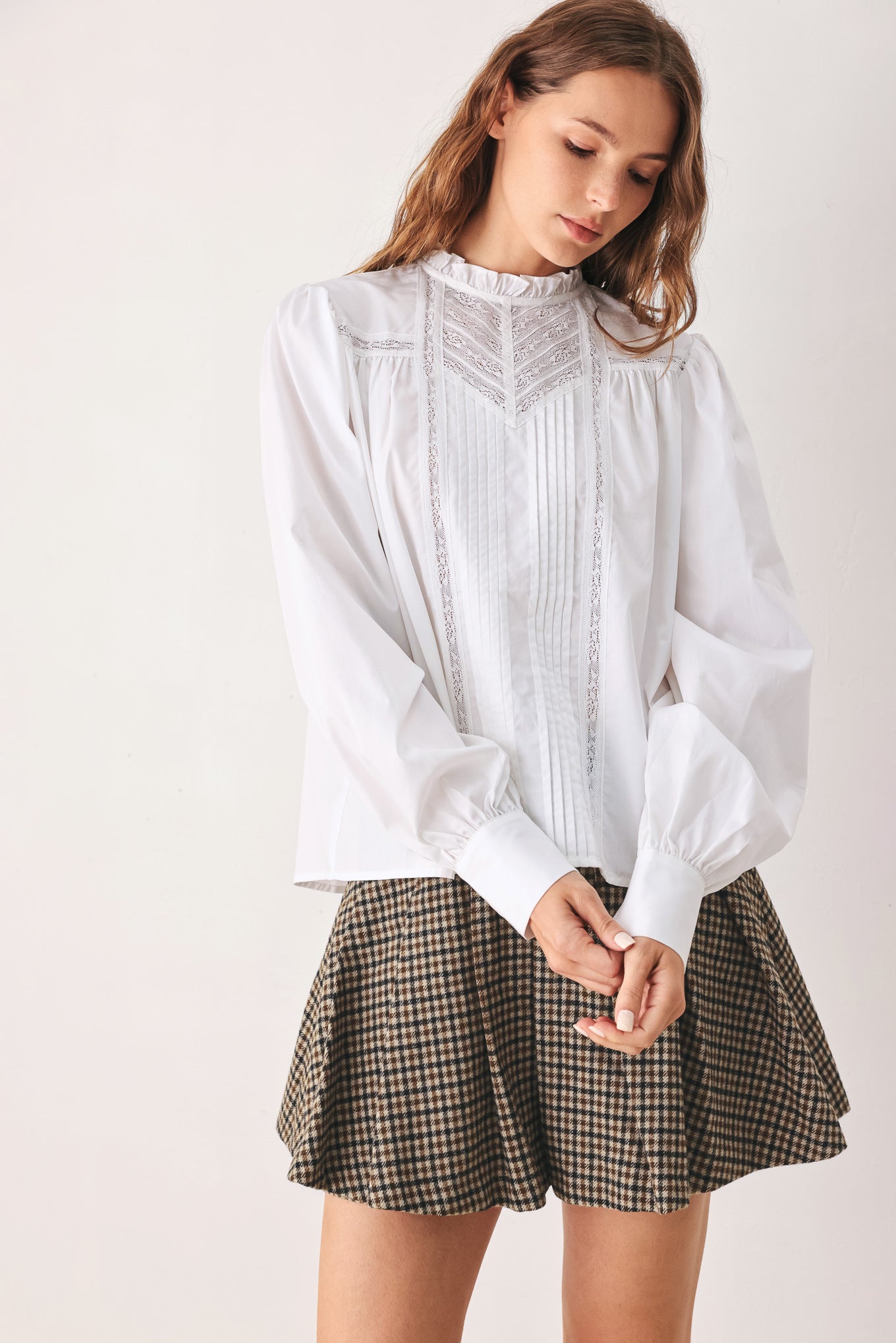 A woman modeling a white long-sleeve blouse with a ruffled high neck, pleated front, and lace detailing | FREEMARKET