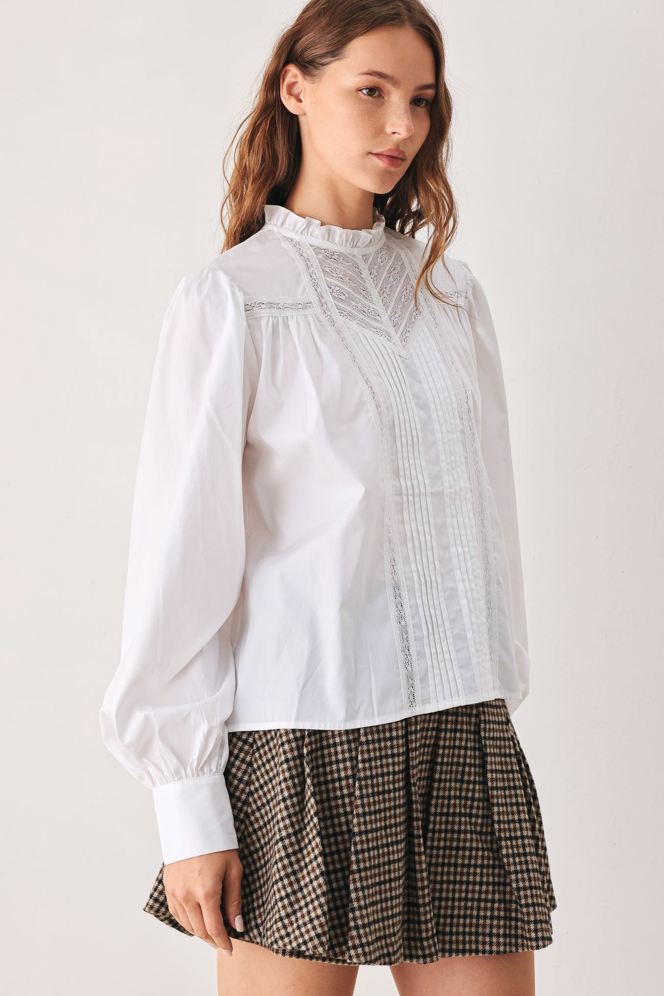 A woman modeling a white long-sleeve blouse with a ruffled high neck, pleated front, and lace detailing | FREEMARKET