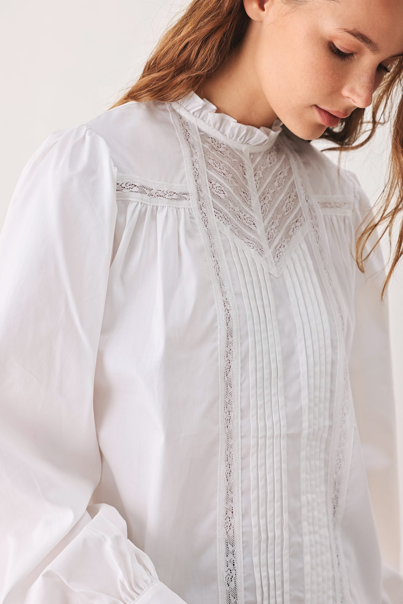 A woman modeling a white long-sleeve blouse with a ruffled high neck, pleated front, and lace detailing | FREEMARKET