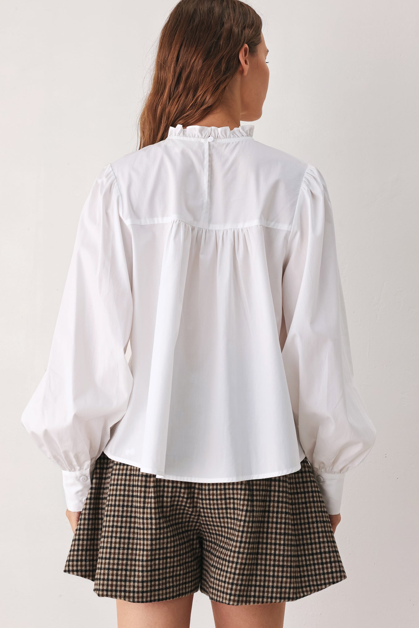 A woman modeling a white long-sleeve blouse with a ruffled high neck, pleated front, and lace detailing | FREEMARKET