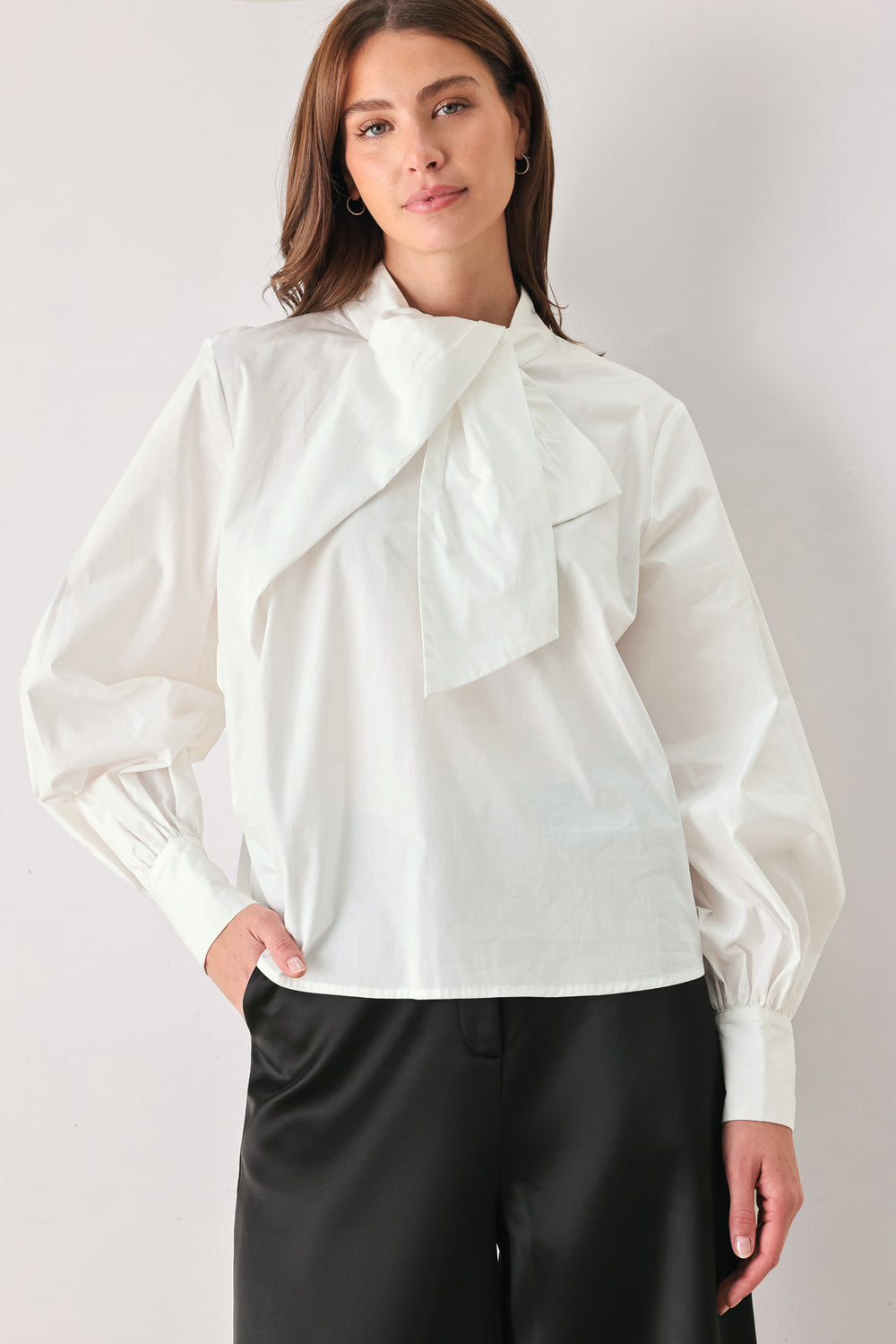 A woman wearing a white long-sleeve blouse with a large draped bow at the collar | FREEMARKET