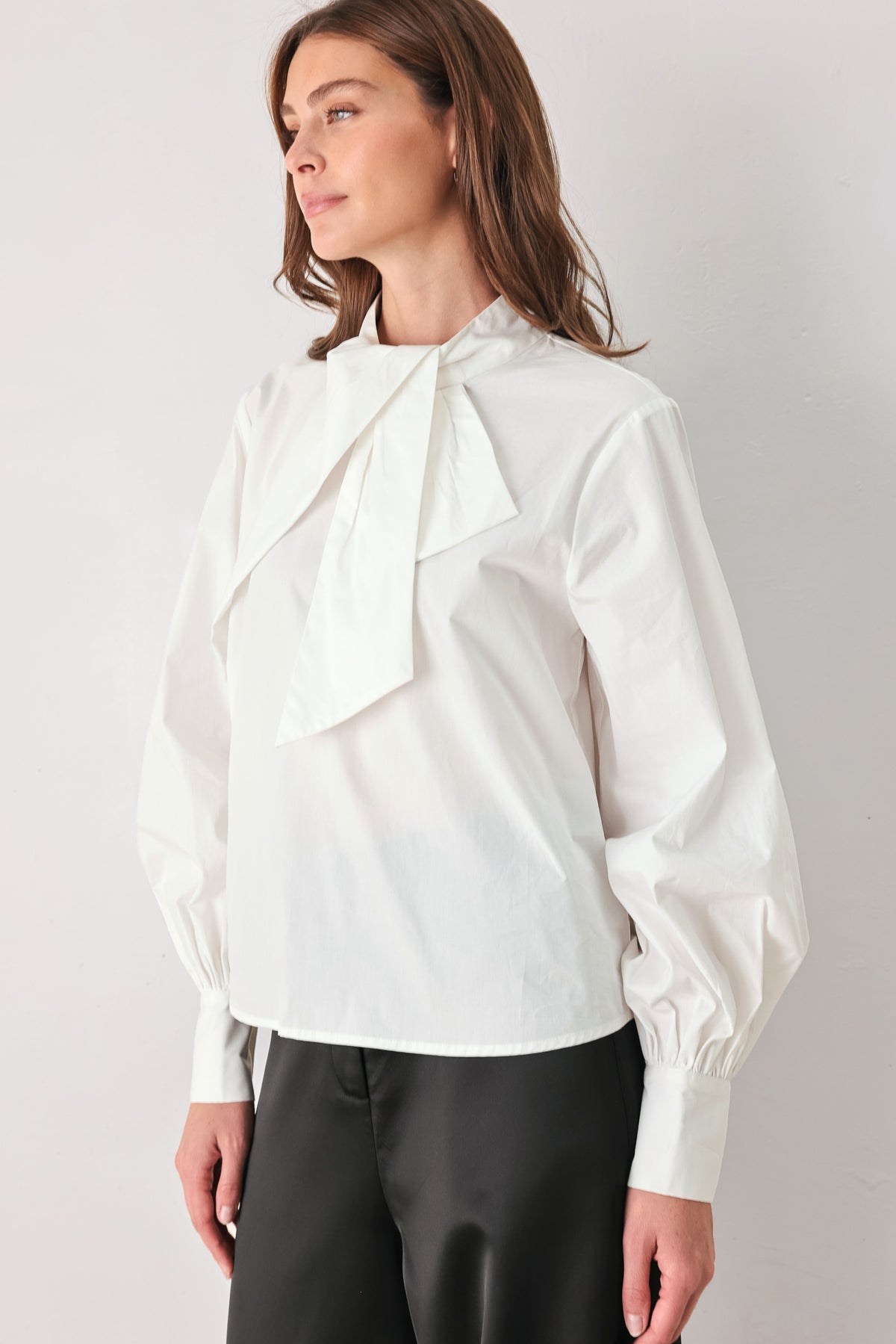 A woman wearing a white long-sleeve blouse with a large draped bow at the collar | FREEMARKET
